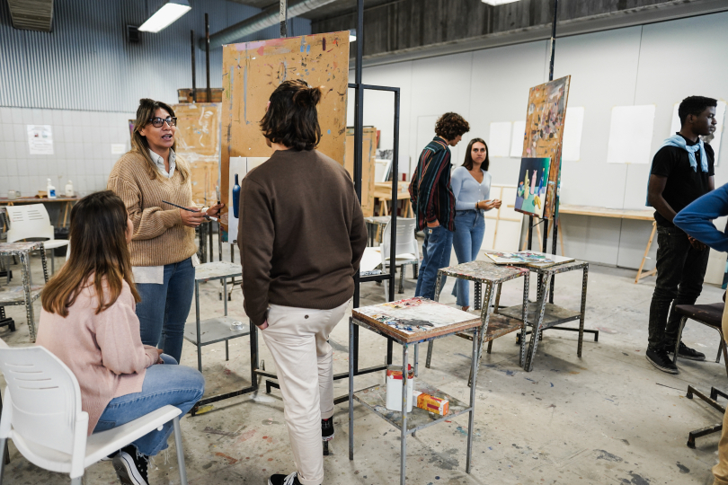 In einem Atelier an Staffeleien sprechen Menschen über Kunst und tauschen sich aus